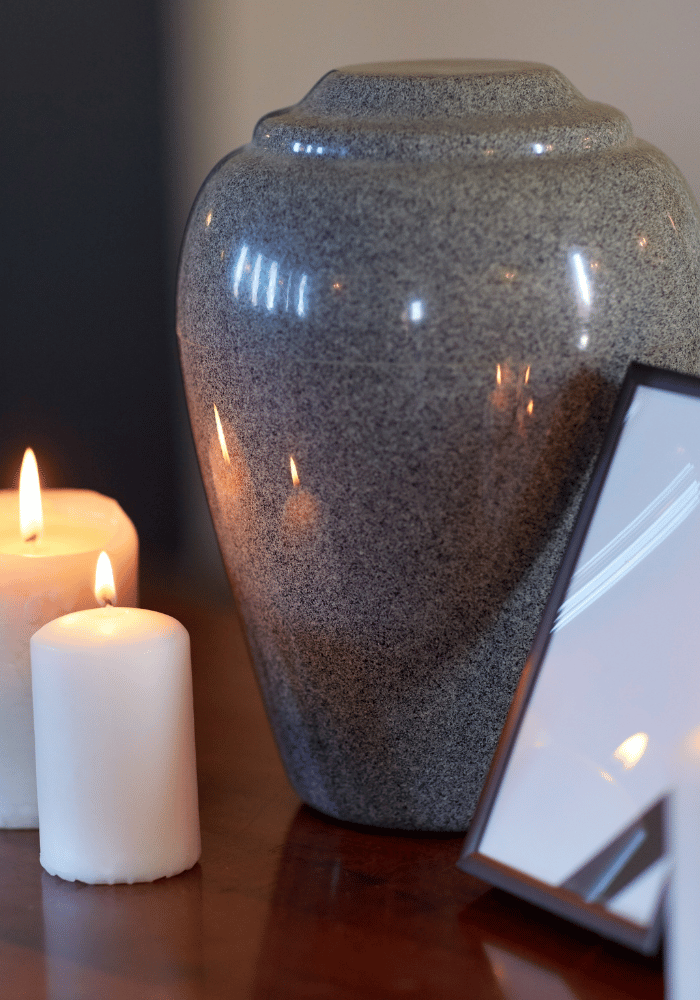 Enzelkremierung. Graue Urne mit Kerzen auf Holztisch.